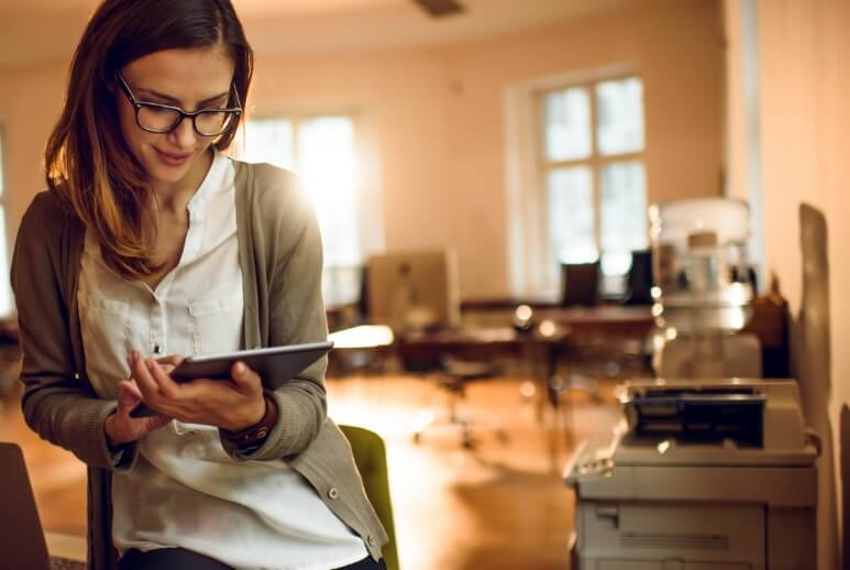 Eine junge Frau liest Dokumente auf Ihrem Tablet. Sie befindet sich in Ihrem Büro und kann so sehr leicht auf die digitalen Unterlagen zugreifen.
