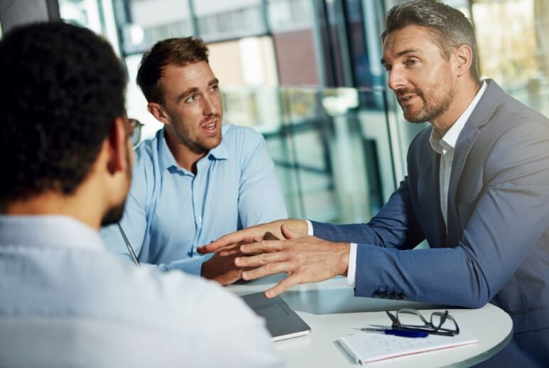 Eine Gesprächssituation dreier Geschäftsmänner, die sich über die betrieblichen Veränderungen in Ihrer IT-Abteilung unterhalten.